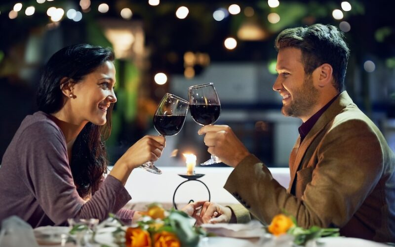 Smile, couple and cheers with wine at restaurant for date, love or holding hands together. Happy man, woman and toast with drink in glass for celebration, anniversary or romance with bokeh at night
